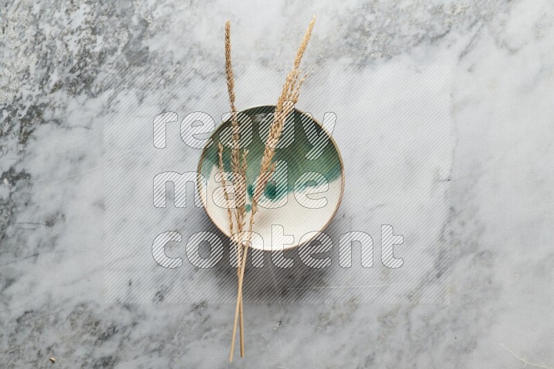 Wheat stalks on multicolored pottery plate on grey marble background
