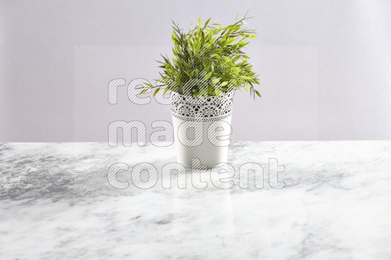 Green artificial plant in white decorative pot on grey marble background