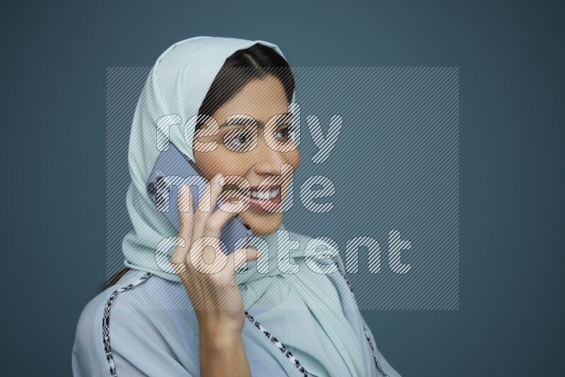 A Saudi woman having a Call in a blue background wearing blue Abaya with hijab