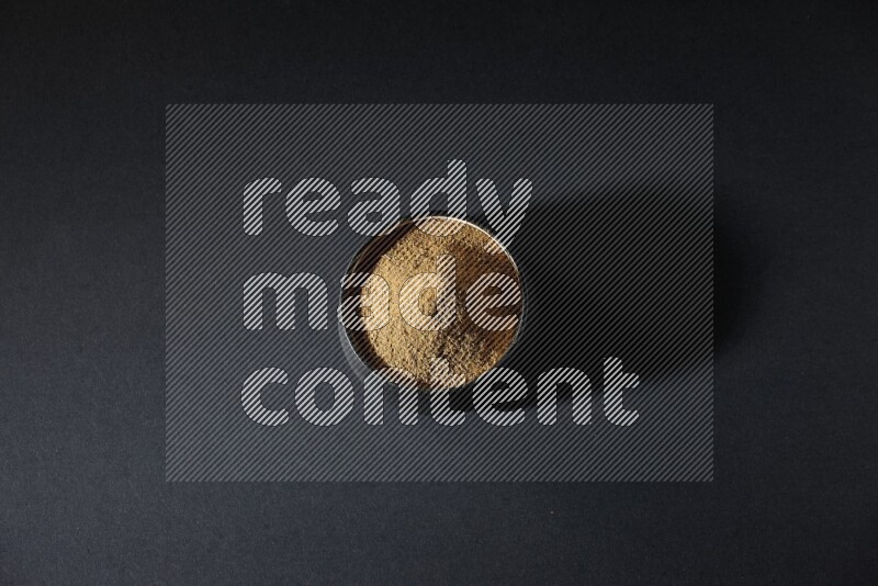 A black pottery bowl full of cumin powder on a black flooring