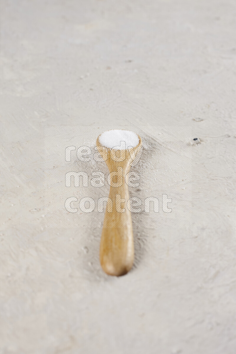 A wooden spoon full of white salt on white background