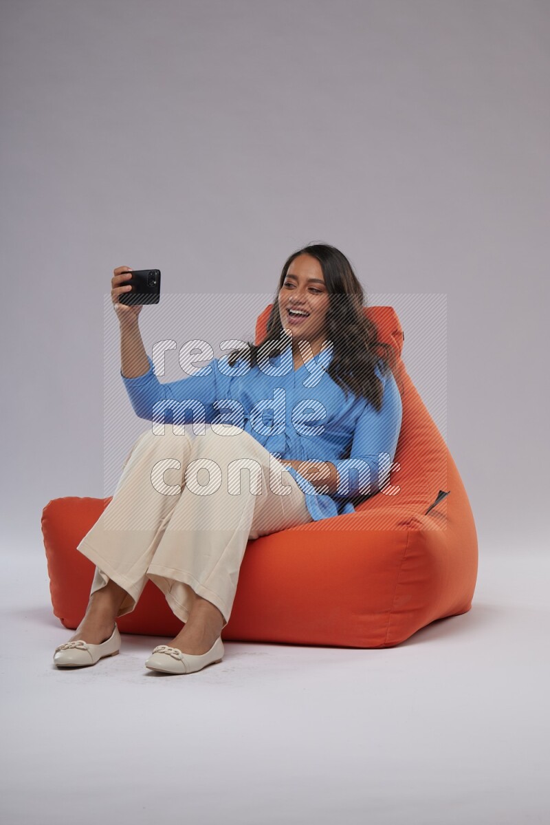 A woman sitting on an orange beanbag and taking selfie