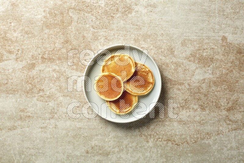 Four stacked plain mini pancakes in a blue plate on beige background