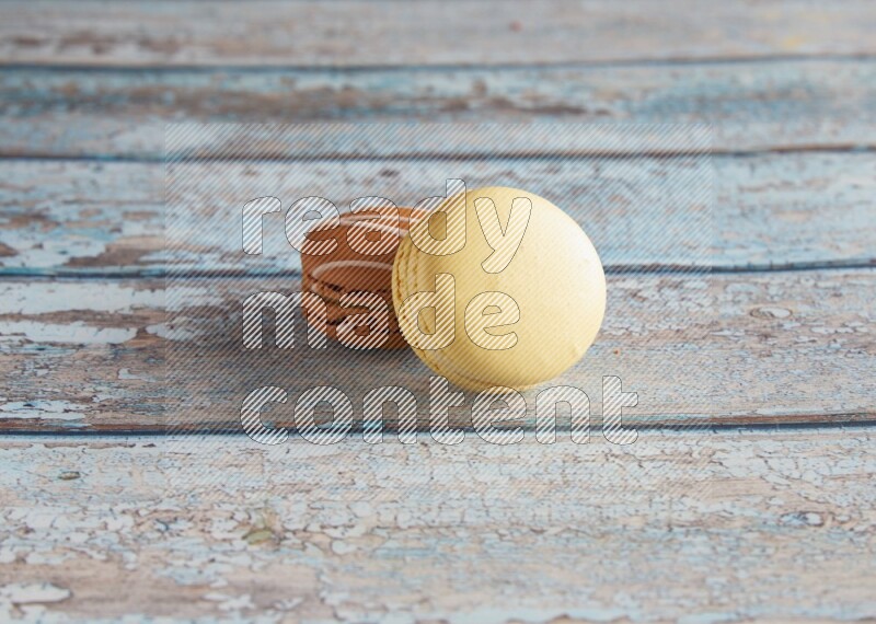 45º Shot of of two assorted Brown Irish Cream, and Yellow Vanilla macarons on light blue background