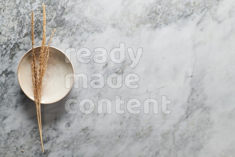 Wheat stalks on beige pottery plate on grey marble background