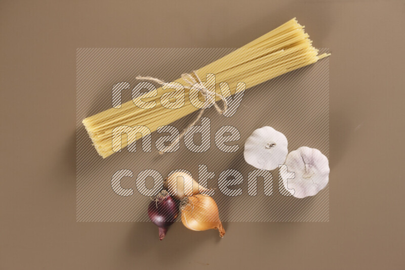 Raw pasta with different ingredients such as cherry tomatoes, garlic, onions, red chilis, black pepper, white pepper, bay laurel leaves, rosemary and cardamom on beige background