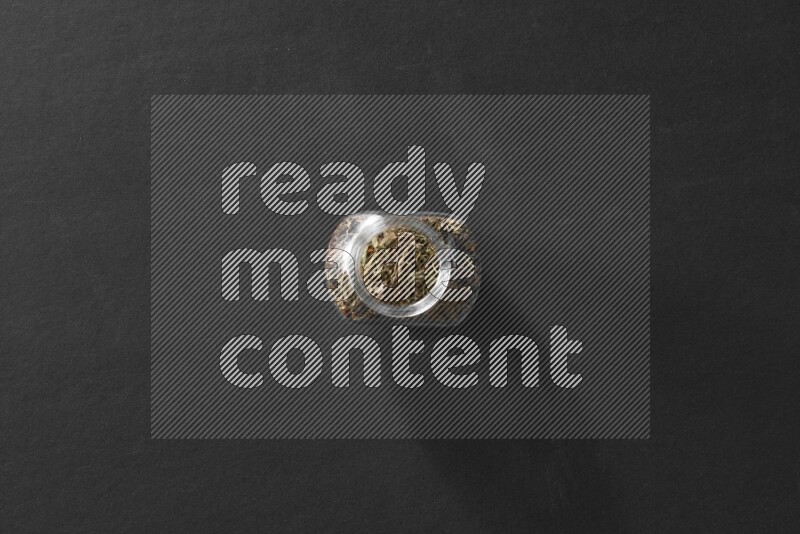 A glass spice jar full of basil on black flooring