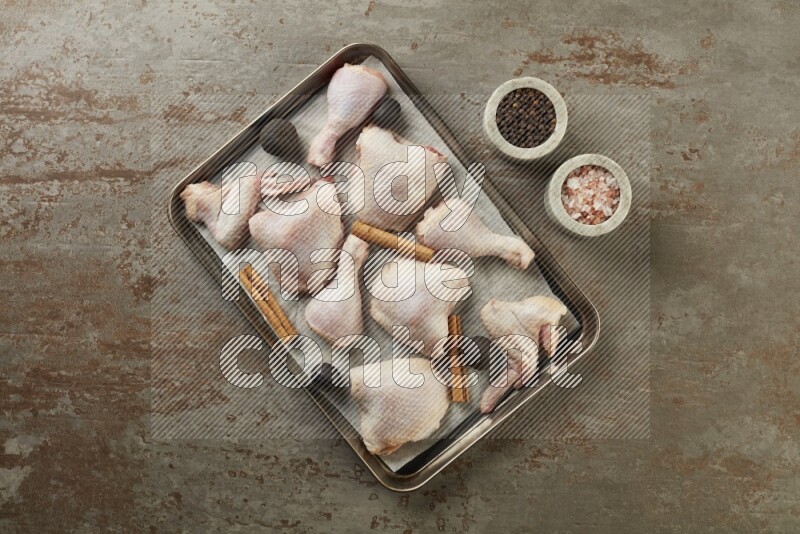 Mixed fresh chicken pieces in an oven tray on a textured rustic background