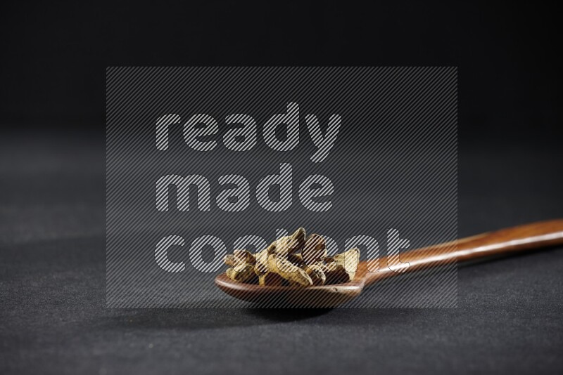 A wooden ladle full of dried turmeric fingers on black flooring