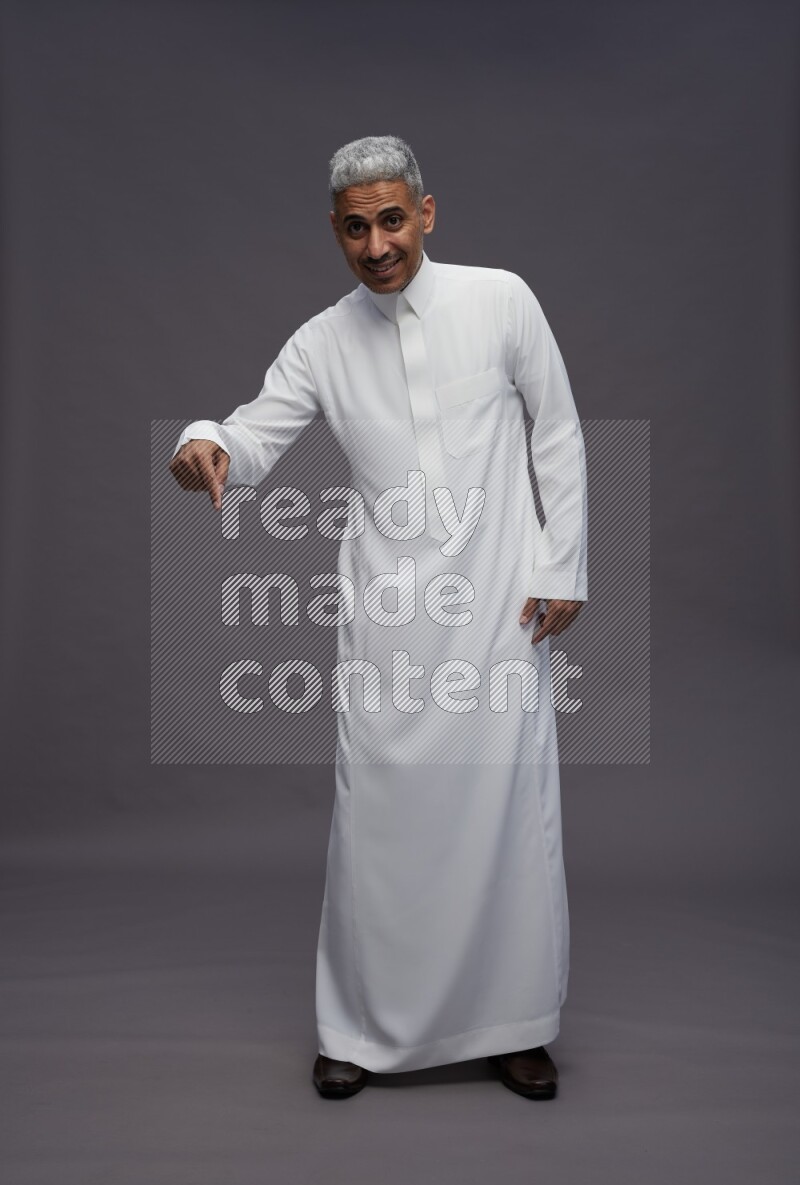 Saudi man wearing thob standing interacting with the camera on gray background