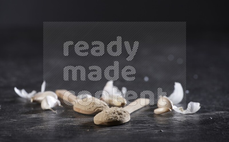 ملعقتان خشبيتان مملوءتان بمسحوق الثوم، محاطتان بفصوص الثوم المقشرة وقشرتها على خلفية سوداء