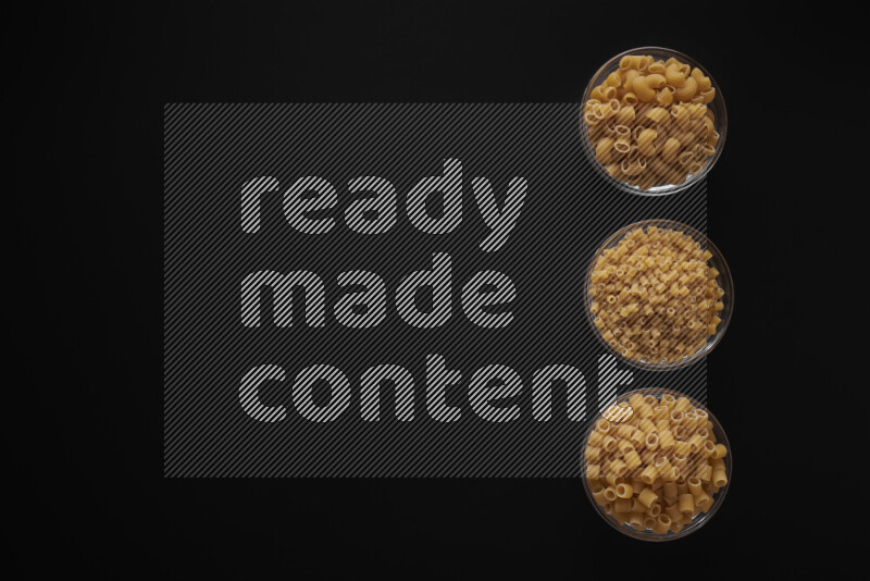 Different pasta types in 3 glass bowls on black background