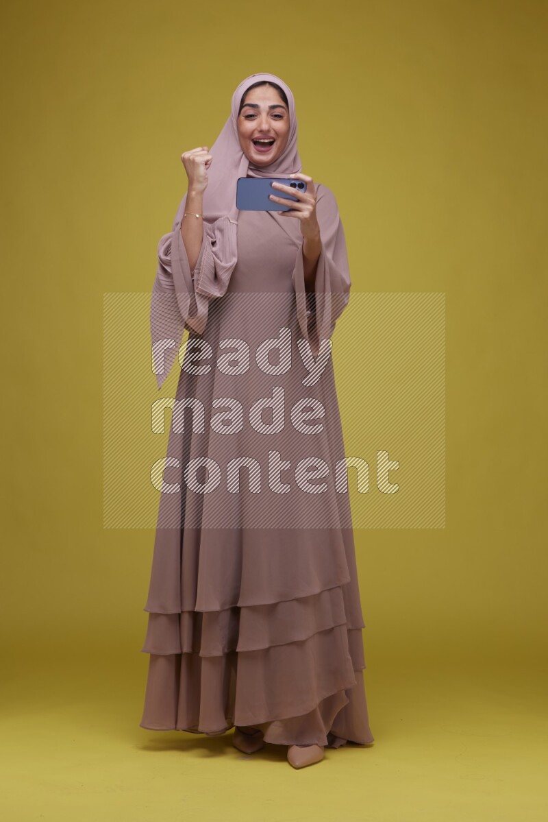 A woman Playing Games a Yellow Background wearing Brown Abaya with Hijab