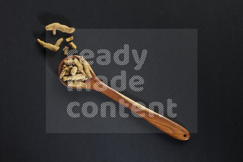 A wooden ladle full of dried turmeric fingers on black flooring