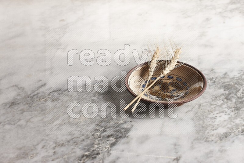 Wheat stalks on decorative pottery plate on grey marble background