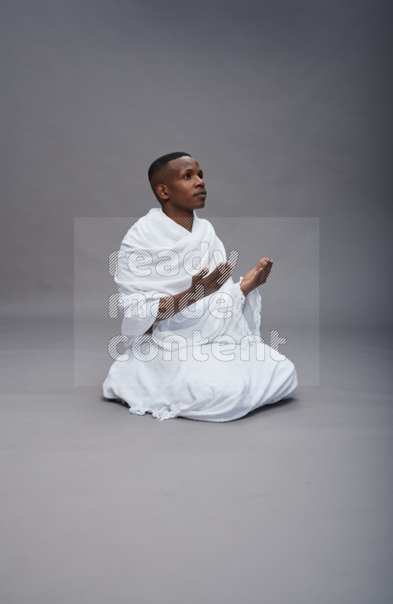 A man wearing Ehram sitting on floor dua'a on gray background