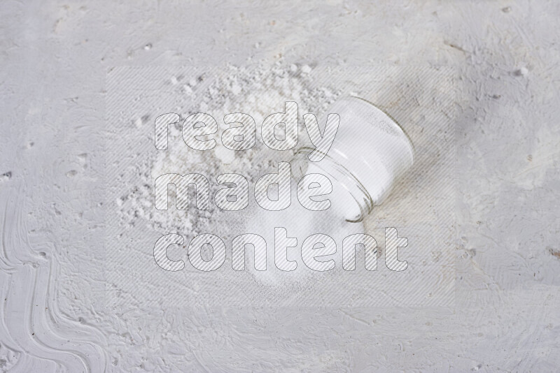 A glass jar full of table salt with some sea salt crystals beside it on a white background