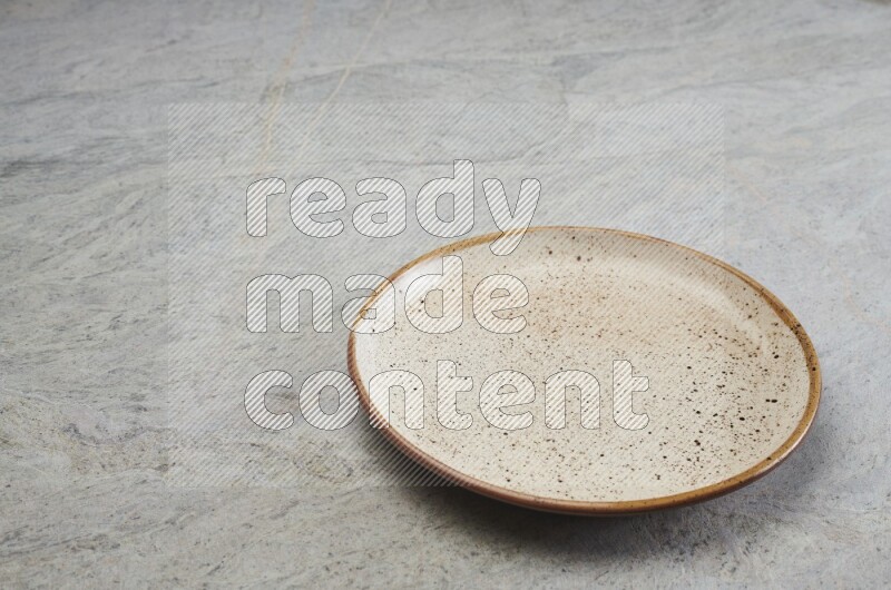 A beige pottery plate on grey marble background