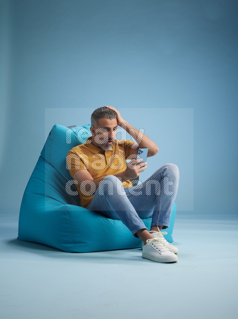 A man sitting on a blue beanbag and texting on phone