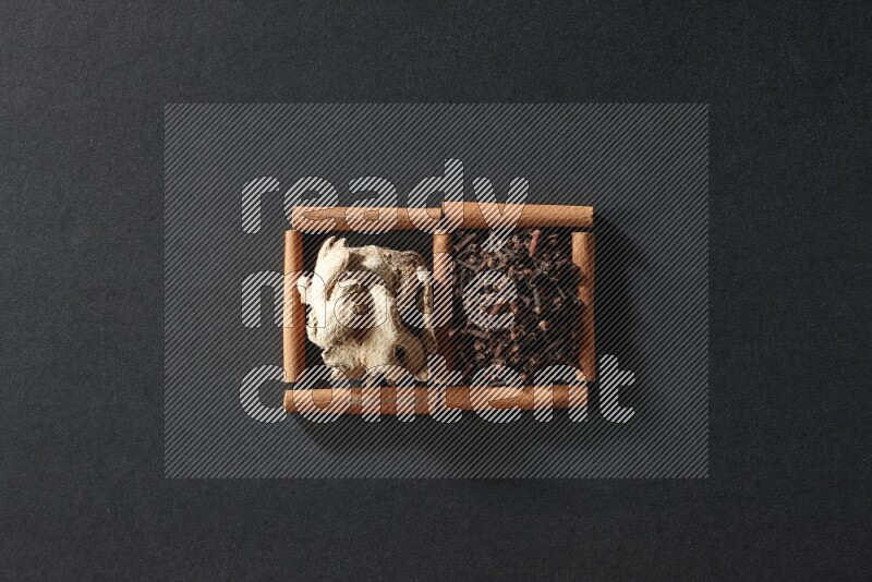 مربعان من أعواد القرفة ممتلئان بالقرنفل والزنجبيل المجفف علي خلفية سوداء