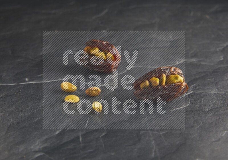 two pistachios stuffed madjoul dates on a black textured background