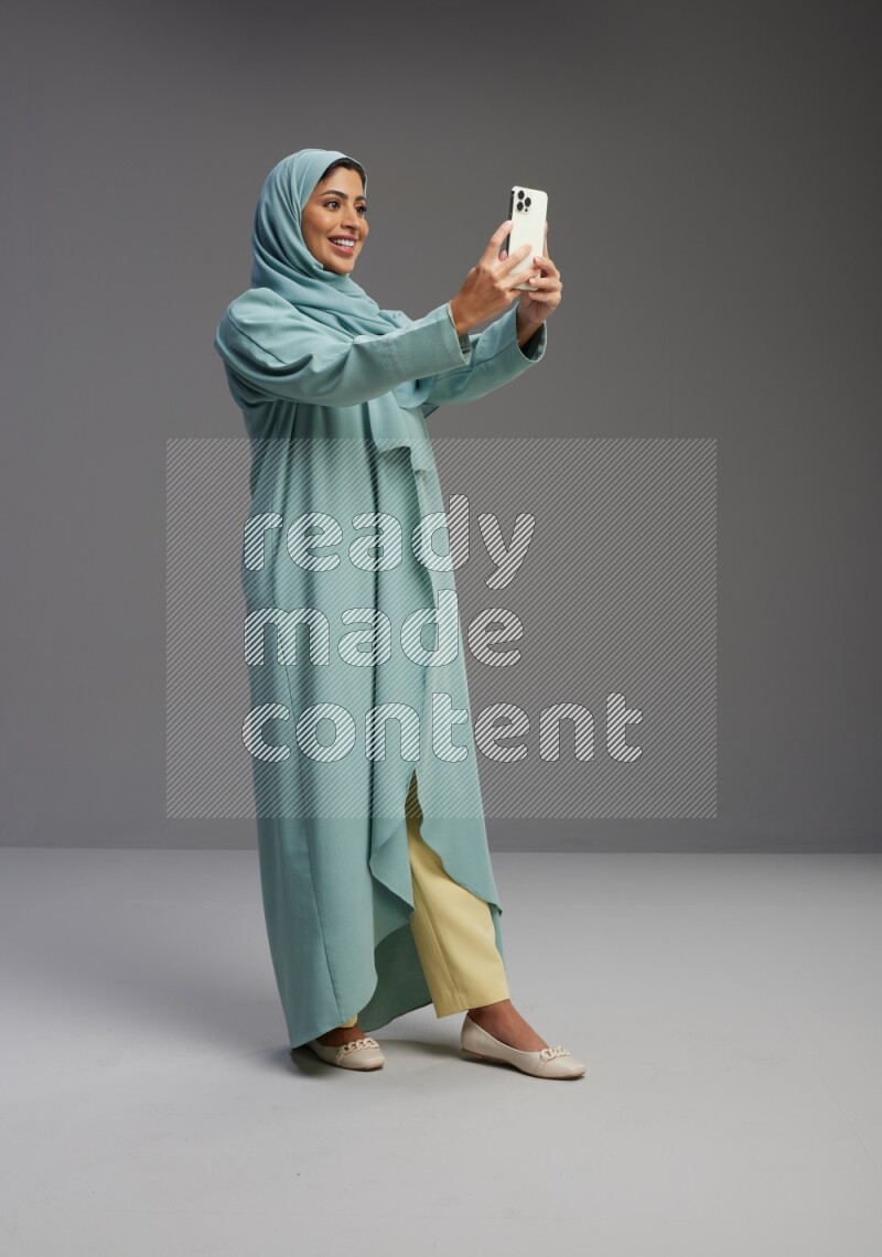 Saudi Woman wearing Abaya standing taking selfie on Gray background