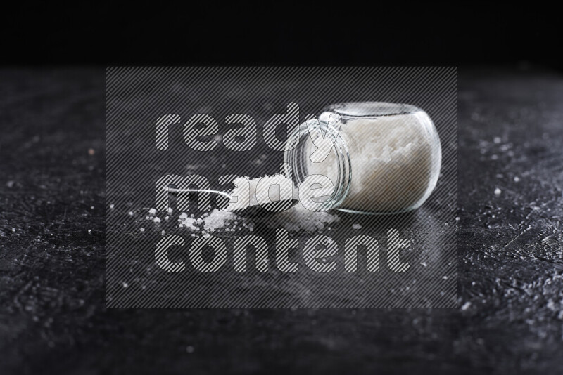 A glass jar full of coarse sea salt crystals on black background