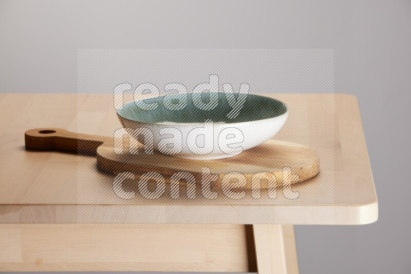 multi colored bowl placed on a  wooden oval cutting board on the edge of wooden table