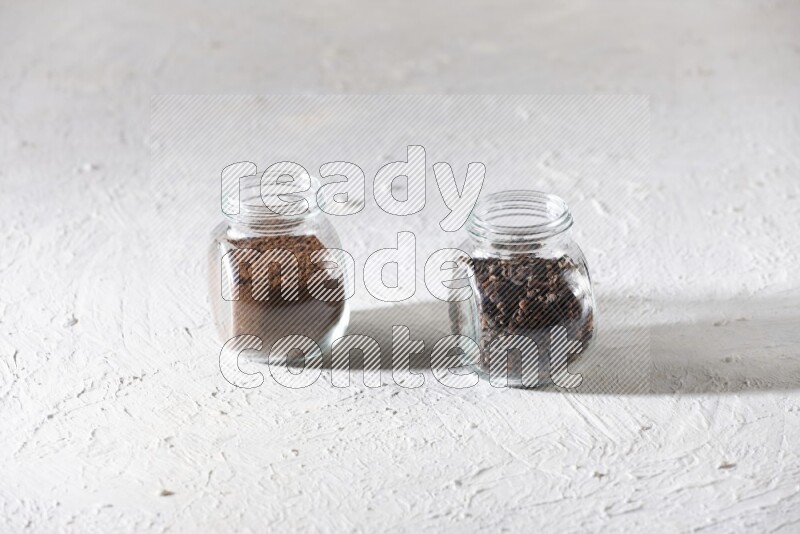 2 glass jars full of cloves powder and cloves grains on a textured white flooring
