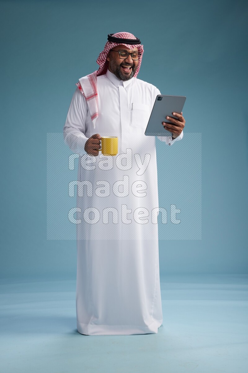 Saudi Man with shimag Standing holding a tablet on blue background