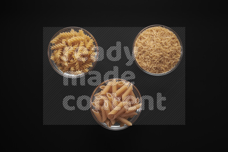 Different pasta types in glass bowls on black background