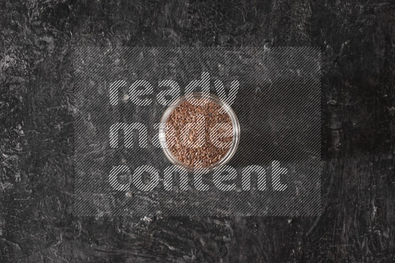 A glass jar full of flaxseeds on a textured black flooring