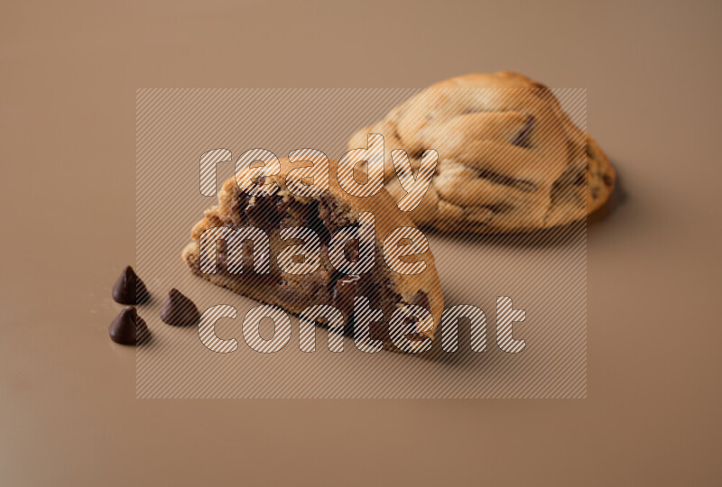 a chocolate chip cookie with another one cut in half on a brown background