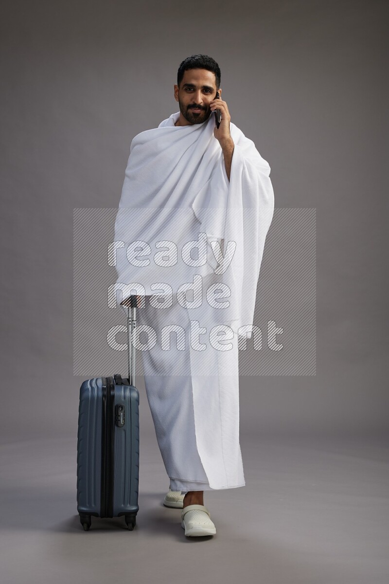 A man wearing Ehram Standing holding traveling bag on gray background