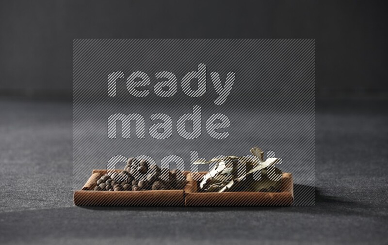 مربعان من أعواد القرفة ممتلئان ببهار الفلفل الحلو وأوراق الغار علي خلفية سوداء