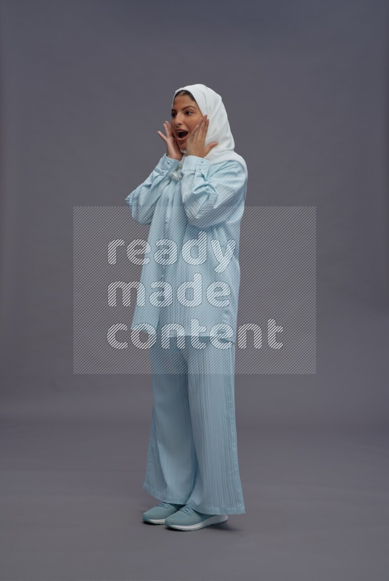 Saudi woman wearing hijab clothes standing interacting with the camera on gray background