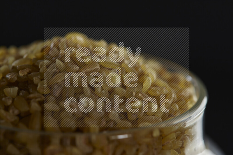 Coarse bulgur in a glass jar on black background