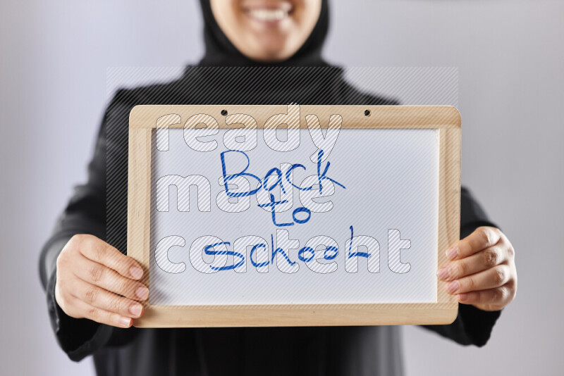 A woman in abaya holding books and a board in different positions (back to school)