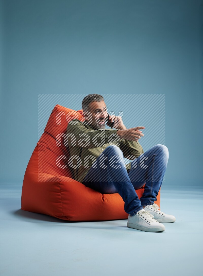 A man sitting on an orange beanbag and talking on the phone