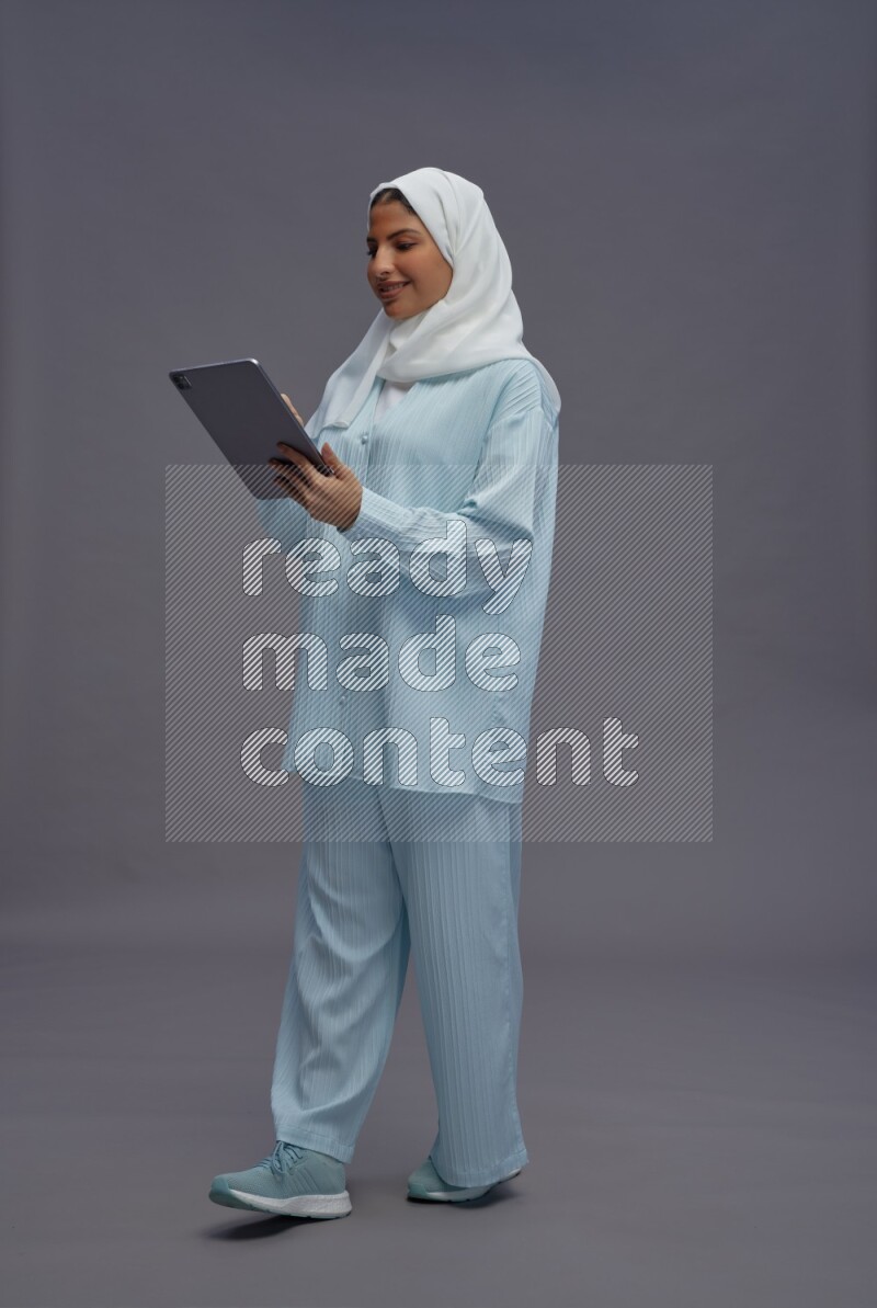 Saudi woman wearing hijab clothes standing working on tablet on gray background