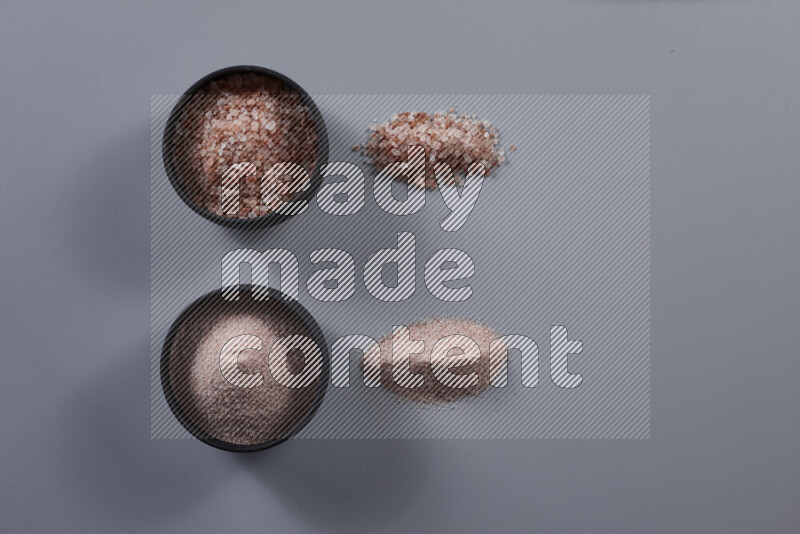 2 وعاء فخاري احدهمها ممتلئ بملح الهيمالايا الناعم والأخر بملح الهيمالايا الخشن على خلفية رمادية