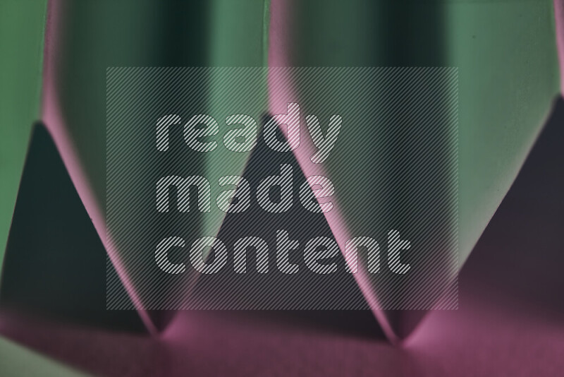 A close-up abstract image showing sharp geometric paper folds in green and pink gradients