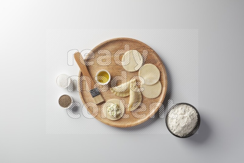 two closed sambosas and one open sambosa filled with cheese while flour, salt, black pepper and oil with oil brush aside in a wooden dish on a white background