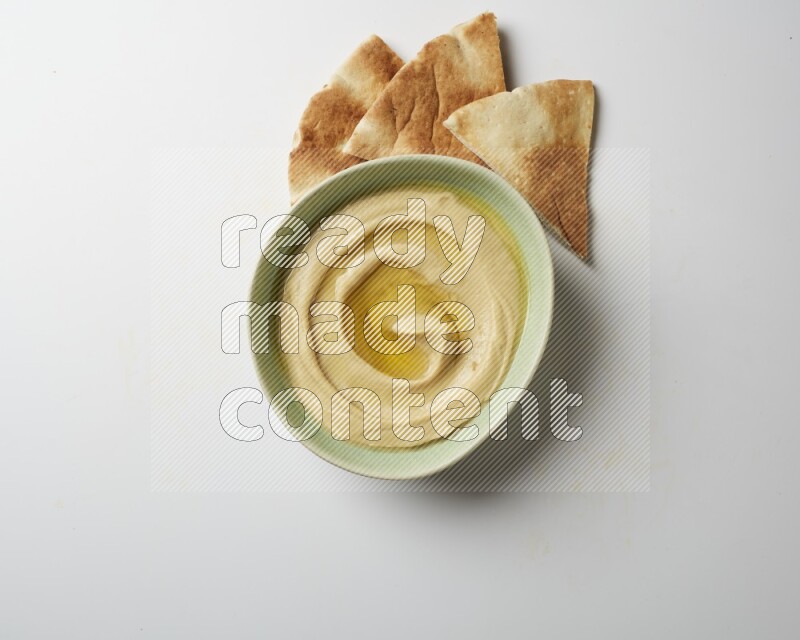 Hummus in a green plate garnished with olive oil on a white background