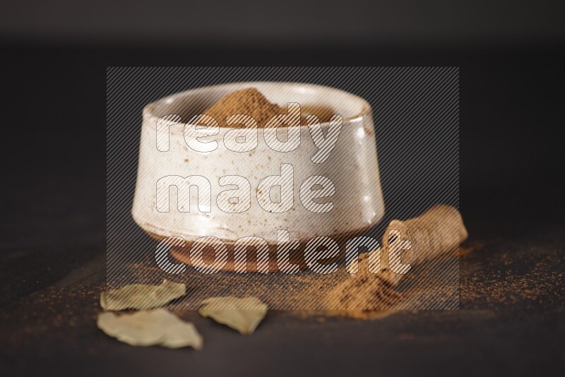 Cinnamon powder in a white pottery bowl and cinnamon sticks and laurel leaves on black background