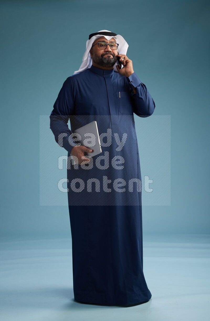 Saudi Man with shimag Standing talking on phone on blue background