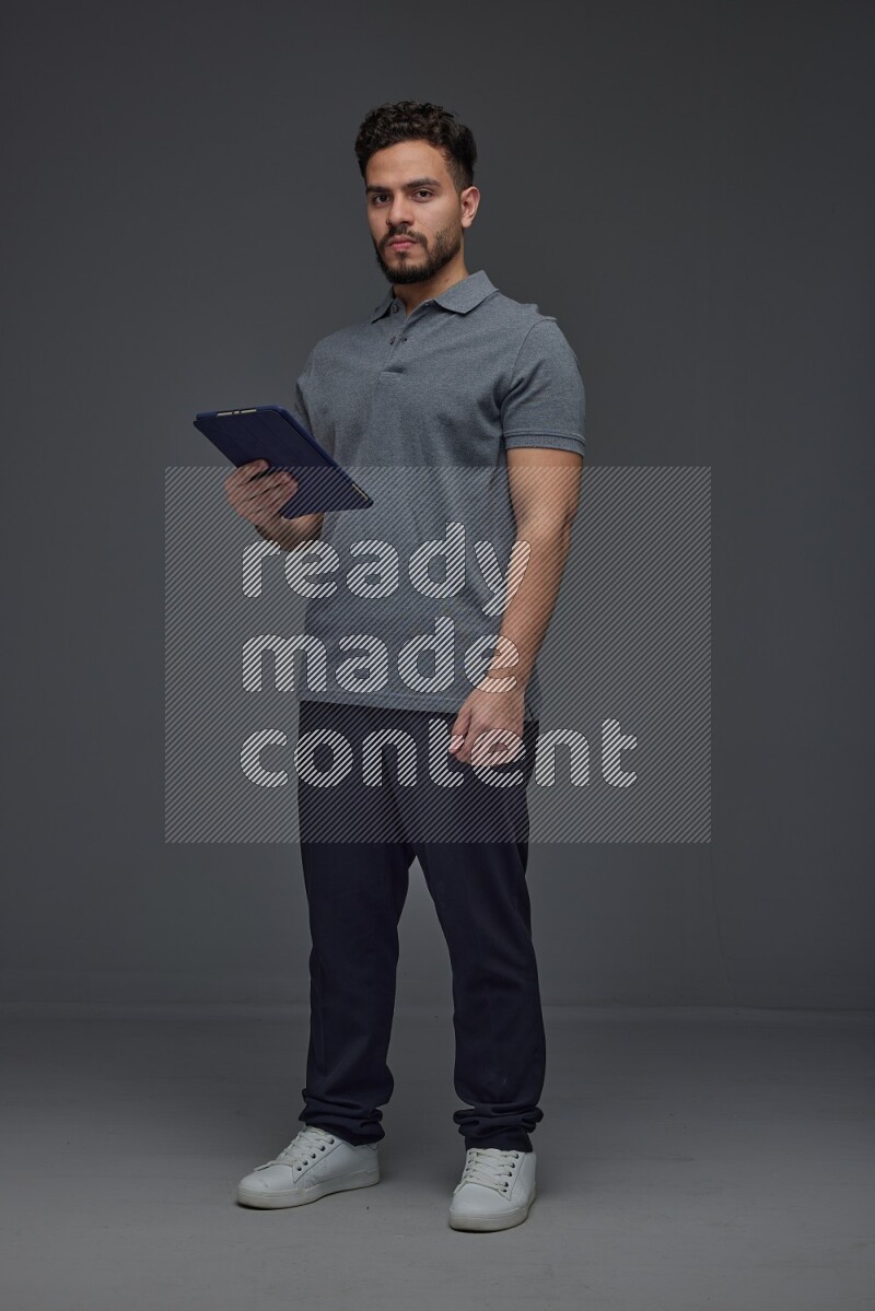 A man wearing casual standing and using his tablet and making multi hand gestures different angles eye level on a gray background