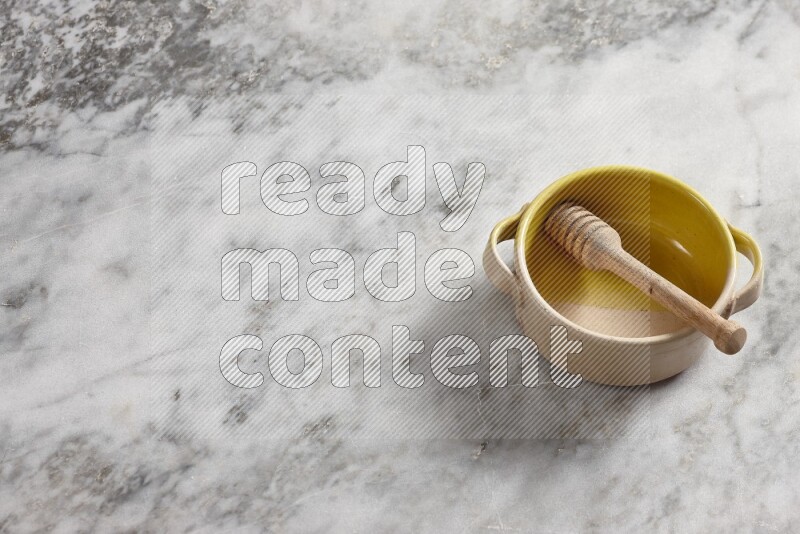 Multicolored pottery bowl with wooden honey dipper in it on grey marble background