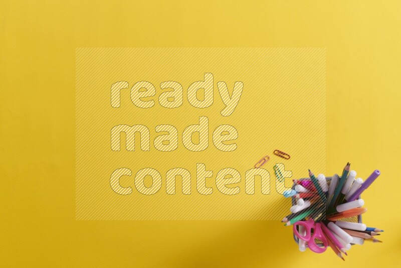 بعض الأقلام والمستلزمات المدرسية في مقلمة معدنية علي خلفية صفراء