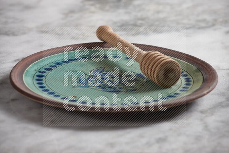 Decorative pottery plate with wooden honey dipper in it on grey marble background